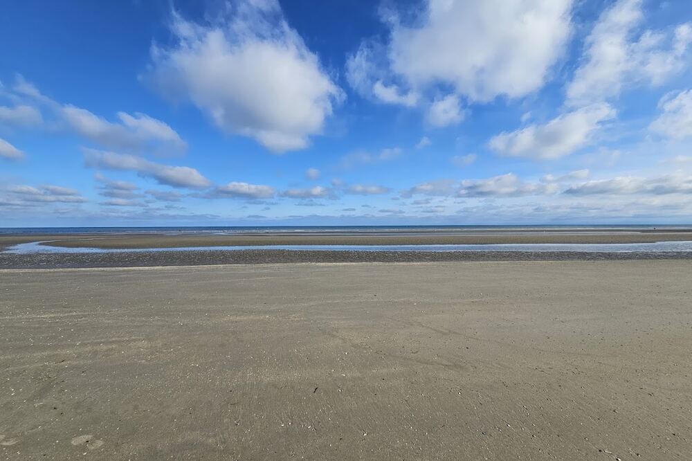 Het brede strand van De Panne onder een wolkenlucht